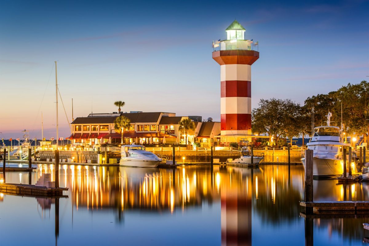 A view of Harbour Town Lighthouse in the evening with lights reflecting on the water